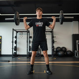 Roll Gear LLC youth black cotton t-shirt with "EARNED NOT GIVEN" graphic, worn by athletes training in a gym.