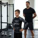 Roll Gear Youth SWAT Edition Short Sleeve Rash Guard, boy standing beside a coach in a gym.