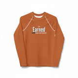 Roll Gear youth long sleeve rash guard in burnt orange with "Earned" graphic. Moisture-wicking, 4-way stretch fabric for BJJ, wrestling, and MMA.