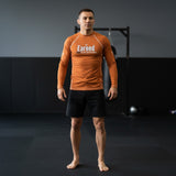 Roll Gear long sleeve rash guard in burnt orange with "Earned Not Given" graphic. Moisture-wicking, 4-way stretch fabric for BJJ, wrestling, and MMA.