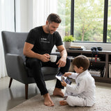 Black heavyweight cotton tee, flat front view, printed “Jiu Jitsu Dad (noun) Full-Time Mat Analyst” in cream.